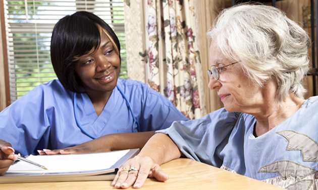 A nursing student smiles as she sits next to a resident in a care home while on placement