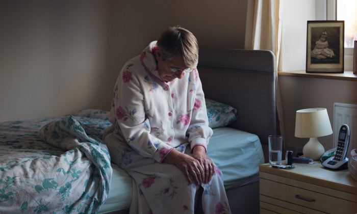 woman sits in her dressing gown on the edge of her bed