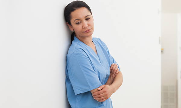Nurse leans on wall looking dejected – as guidance aims to help NHS staff address workplace bullying