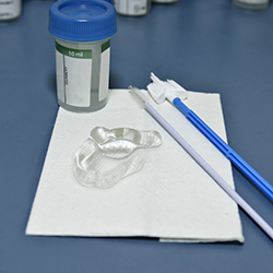 A photo of smear test equipment – two brushes, a plastic speculum and a pot to colllect cells