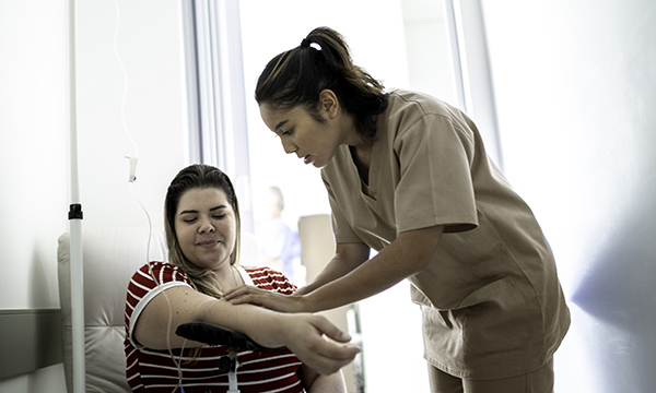 Nursing associate works with seated patient's IV line – the band 4 role is being considered for Wales’s NHS