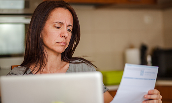 A woman sitting at a computer frowns as she holds up a bill