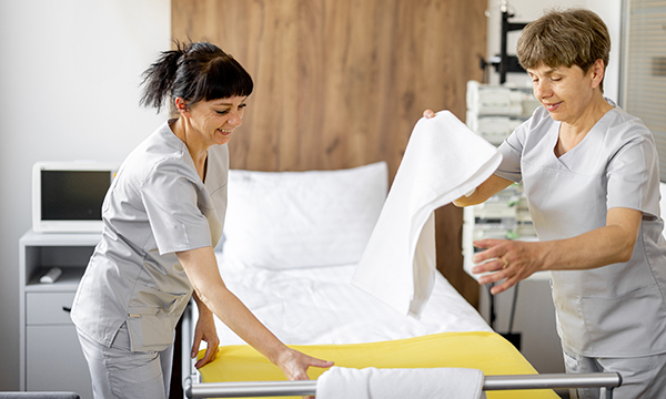 Nursing support staff play an essential role, but inflated job titles may hide over-reliance on them. Image shows two support staff making a bed in a hospital ward