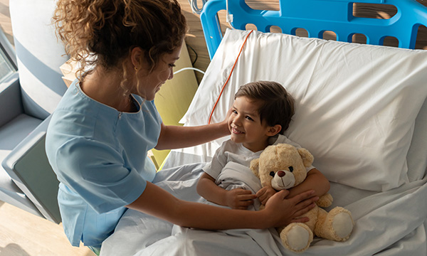 Children’s hospice care:&nbsp;children are living longer, with more complexity and technology dependence than ever before: a nurse comforts a child with a teddy bear in a hospice bed