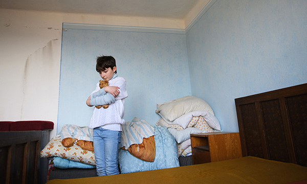 Alt pic text: 4.3 million children in the UK are now living in poverty according to the Joseph Roundtree Foundation: a sad child clutches a teddy bear in a cramped and dingy bedroom