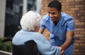 Social care placement: a nurse cares for a care home resident in a wheelchair as they converse in the outdoor area of the facility