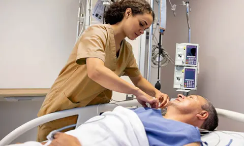 A nursing associate in training cares for a patient in a hospital bed