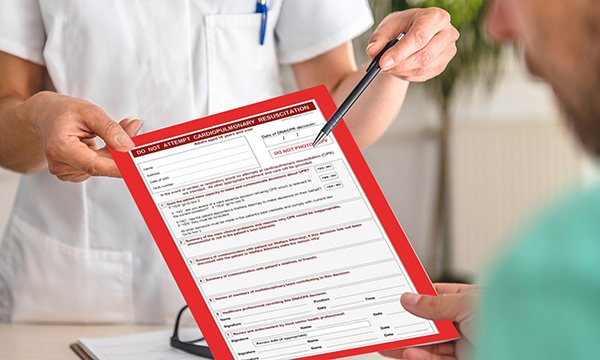 Picture shows a man looking at a DNACPR form and a female medic offering a pen for him to sign it