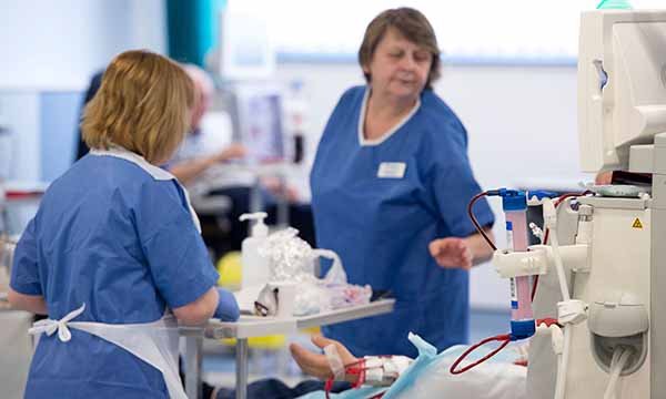 Two nurses give care at the bedside of patient in a high-intervention setting – as survey suggests short-staffing is harming care