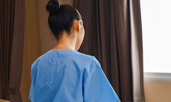 A female nurse looks downwards towards a window: a study is going to examine why female nurses are at higher risk of committing suicide