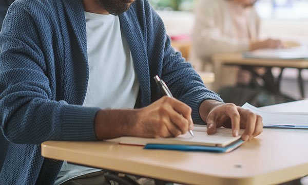 Nurse struck off for exam cheating: man writing notes during a written exam