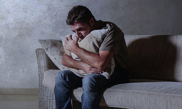 An isolated man hugs a pillow on a sofa. Mental healthcare and distress: Lack of nursing experience and confidence to manage distress can lead to a dependence on restraint, seclusion and/or enhanced observations