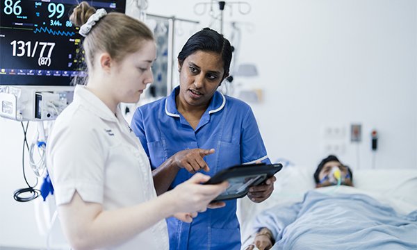 Assessing patient deterioration: nurse and nursing student confer over patient’s observations near patient’s bedside