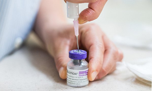 Hands shown drawing substance into a syringe from bottle labelled 'Botox'